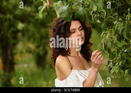 Eine junge Frau mit lockigen Haaren genießt die Natur, während sie ein schönes Sommerkleid im Park trägt. Stockfoto