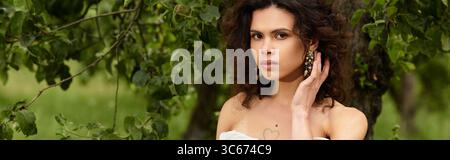 Lockenhaarige Frau in einem weißen Sommerkleid umarmt die Natur in einem ruhigen Dorfpark, Banner Stockfoto