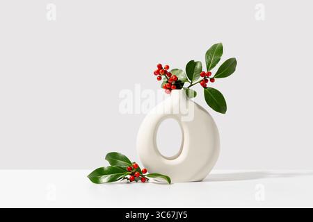 weihnachtsbaum mit roten Beeren in weißer Vase. Natürliche Winterdekoration auf weißem Hintergrund, Kopierraum. Stockfoto