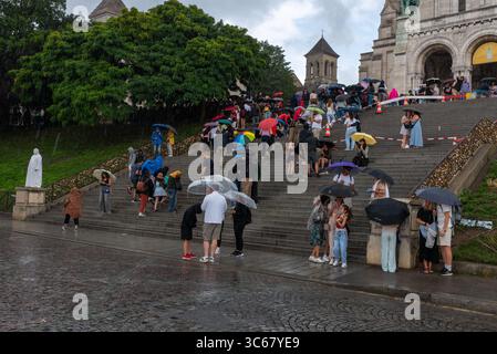 Touristen finden bei starkem Regen in Montmartre Unterschlupf unter Regenschirmen. Starkregen in Paris an einem heißen Sommertag. Montmartre Treppe Stockfoto