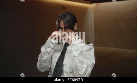 Frau boxt im Innenraum in Pilotenuniform, zeigt Selbstvertrauen, Stärke und Entschlossenheit. Stockfoto