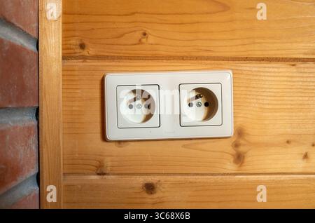 Zwei weiße Steckdosen an einer Holzwand. Die Steckdosen sind nicht mit irgendeinem verbunden. Die Mauer ist aus Holz und hat eine gemauerte Umrandung Stockfoto