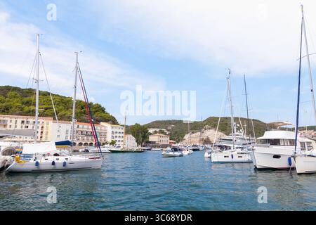 Bezaubernde Yachthafenszene mit Segelbooten vor einer natürlichen Hügellandschaft unter blauem Himmel, die eine ruhige Küstenatmosphäre schafft. Bonifacio, Stockfoto