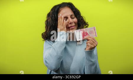 Eine Frau, die isländische Krone hält, scheint vor einem hellgelben Hintergrund besorgt zu sein. Stockfoto