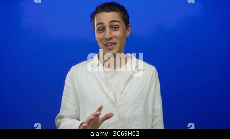 Junger Mann in weißem Hemd, der vor einer leuchtend blauen Hintergrundwand spricht Stockfoto