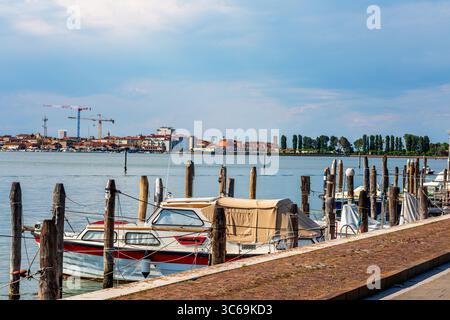 Malerischer Blick auf das Wasser mit Holzpfosten und einem Boot, das das ruhige Wasser unter einem klaren blauen Himmel mit weichen Wolken reflektiert und eine ruhige Atmosphäre bietet Stockfoto