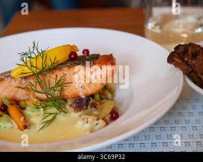 Ein wunderschön überzogenes gegrilltes Lachsfilet mit Kräutern und Gemüse, serviert auf einem weißen Teller in einem Restaurant. Stockfoto