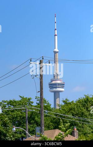 Der CN Tower erhebt sich über Baumlinien und Dächern, umrahmt von Versorgungsmasten und Stromleitungen unter einem klaren blauen Himmel. Stockfoto