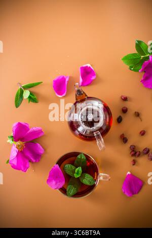 Ästhetische Teeschichtung mit Hagebutte, Blüten und Minzgrün auf braunem Hintergrund. Stockfoto