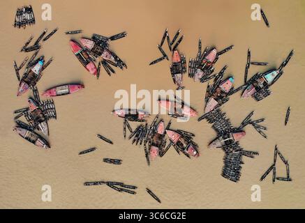 Aus der Vogelperspektive sehen Sie bunte Boote, die sich auf dem schlammigen Jadukata-Fluss ansammeln, deren Reflexionen auf dem Wasser glitzern, Barek Tila, Sylhet Division, Bangladesch. Stockfoto