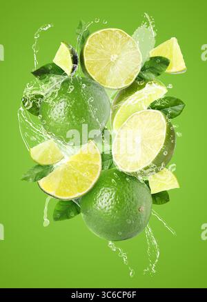 Frische Limetten und Spritzwasser in der Luft vor grünem Hintergrund Stockfoto