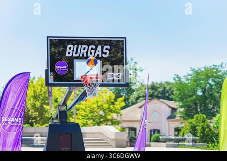 Basketball trifft den Ring. Basketball, der während des 3x3 SESAM-Turniers in Burgas durch den Korb schwingt, mit hellen Fahnen im Hintergrund. Konzept von Stockfoto