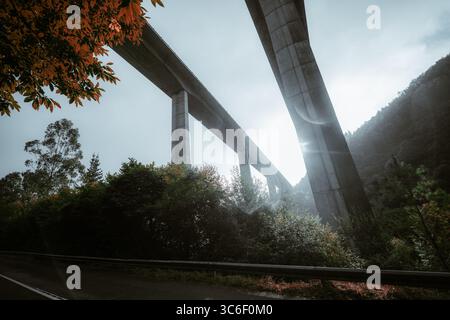Dramatische Weitwinkelansicht einer hohen Straßenbrücke aus Beton, die bei leichtem Regen von unten aufgenommen wurde, mit Objektivfackeln, sichtbaren Regentropfen und sanftem Glühen-Addin Stockfoto