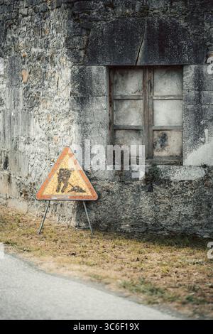 Verwittertes Bauwarnschild vor einem alten Steingebäude mit versiegeltem Holzfenster, das einen starken Kontrast zwischen modernen infras schafft Stockfoto