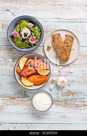 Studio-Aufnahme von Hummer-Klauen aus Farmfood, serviert mit hausgemachtem Sauerteig, grünem Salat und essbaren Blumen aus dem Garten. 🏷️ Schlüsselwörter (Rechte M Stockfoto