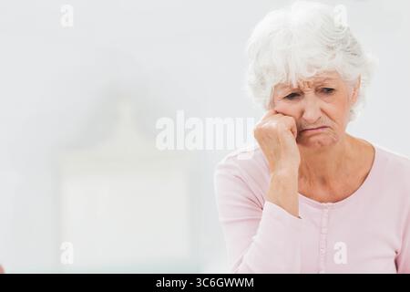 Ältere Frau, die sich nach vorne beugt, mit der Hand im Wohnzimmer neben der Tischlampe, Kopierraum. Reflexion, Introspektion, Gelassenheit, Komfort, Coz Stockfoto