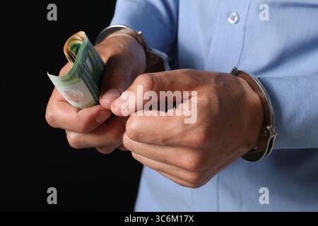Korruption. Mann in Handschellen, der Euro-Banknoten auf schwarzem Hintergrund hält, Nahaufnahme Stockfoto