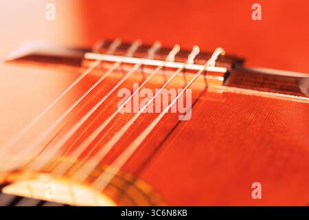 Warmes Licht auf der Brücke der klassischen Gitarre, das die glatten Nylonsaiten und die satte Holzmaserung freigibt. Die Nahaufnahme zeigt das elegante Handwerkskunst des Instruments Stockfoto