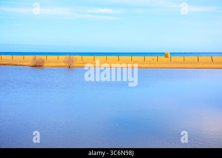 Lebendige Küstenszene mit einem ruhigen Gewässer im Vordergrund und einem goldenen Sandstreifen, der zum tiefblauen Meer führt. Ruhige Küstenlandschaft Stockfoto
