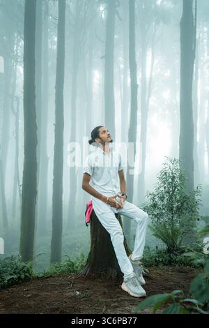 Selbstporträt eines Mannes, der auf einem Baumstumpf in einem nebeligen Wald in Darjeeling, Indien sitzt. Erfasst während der Monsunsaison mit weicher Lichtfilterung. Stockfoto