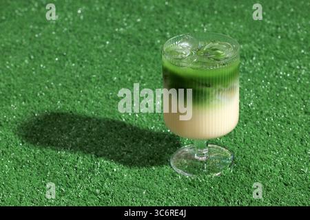 Gefrorener Matcha Latte auf grünem Gras Hintergrund, serviert in Stängelglas Stockfoto