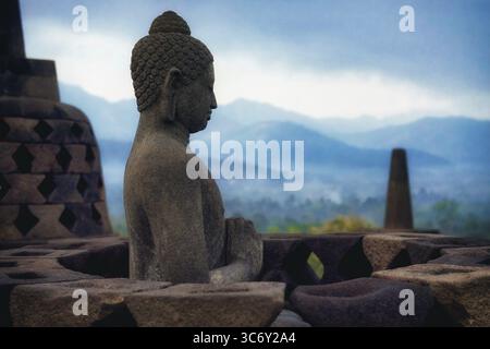 Eine Buddha-Statue in Stein mit Bergen im Hintergrund, Candi Borobudur, Borobudur, Java, Indonesien Stockfoto