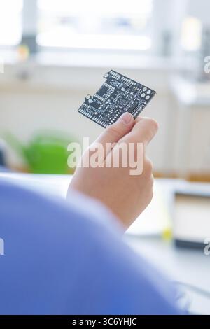 Die Hand hält eine Leiterplatte vor einem verschwommenen Hintergrund, das Fenster leuchtet ein Stockfoto