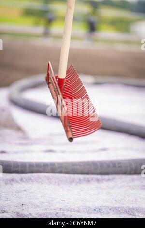 Ein freischwebender roter Rechen vor einem Dach mit verschwommenem Hintergrund in einer Baustellenumgebung, Dachbegrünung, Hausbau, Klima n Stockfoto