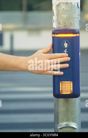 Fußgänger drückt die Taste an der Stadtüberquerung, um die Ampel, vertikales Foto, zu aktivieren. Smart City: Barrierefreiheit zur Förderung der urbanen Mobilität Stockfoto