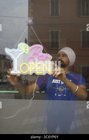 Eine Person stellt ein Neonschild mit der Aufschrift „Bar Open“ an einem Fenster ein, das eine nächtliche Atmosphäre widerspiegelt, Cremona, Italien, 25. Juli 2025 Stockfoto