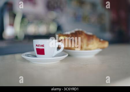 Espresso-Tasse mit Logo und Croissant auf einer Theke, die eine professionelle und einladende Coffee-Shop-Präsentation schafft, Cremona, Italien, 25. Juli 2025 Stockfoto