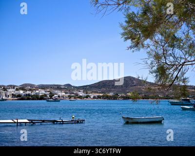 Kleiner Hafen in der Nähe von Adamas auf der Insel Milos, Griechenland, mit Booten, die auf türkisfarbenem Wasser in einer ruhigen Küstenbucht unter Sommersonne schwimmen. Stockfoto