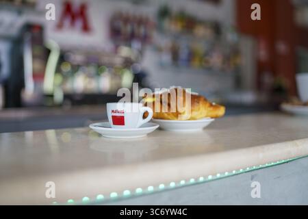 Eine Tasse Espresso neben einem Croissant auf einem Kaffeekocher, mit verschwommenem Hintergrund, der eine gemütliche Atmosphäre schafft, Cremona, Italien, 25. Juli 2025 Stockfoto