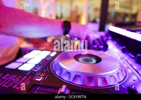 DJ an einem Mischpult mit Fokus auf Plattenspieler, Hand an der Steuerung in bunter Licht und Partyatmosphäre, Close-up, Köln, Nordrhein-Westfalen, Stockfoto