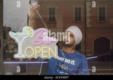 Eine Person installiert ein Neonschild „Bar Open“ an einem Fenster, das eine städtische Umgebung reflektiert, Cremona, Italien, 25. Juli 2025 Stockfoto