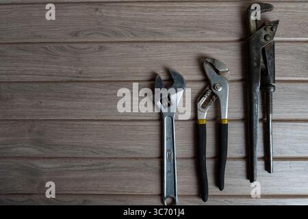 Drei Handwerkzeuge aus Metall – ein Rohrschlüssel, ein verstellbarer Schraubenschlüssel und eine Gleitgelenkzange – sind auf einem verwitterten Holzhintergrund angeordnet Stockfoto