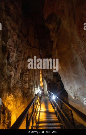 Beleuchtete Felsformationen schaffen eine fesselnde Atmosphäre in einer unterirdischen Höhle. Ein hölzerner Pfad führt Entdecker durch den schmalen Durchgang, h Stockfoto