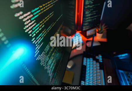 Neonleuchten für den Arbeitsbereich des Programmiergeräts. Nahaufnahme moderner Computerbildschirm mit farbenfrohem Programmiercode, beleuchtet von blauem und rotem Ambie Stockfoto