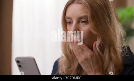 Ängstlich enttäuscht kaukasische Frau liest negative Nachrichten Handy Bankrott im Schlafzimmer Frau hält Smartphone Dame fühlt sich besorgt frustriert Stockfoto