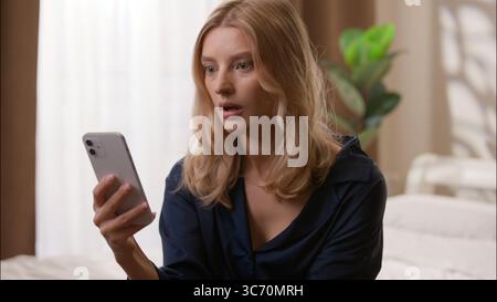 Schockiert enttäuscht kaukasische Frau liest schlechte Nachrichten Handy Problem im Schlafzimmer Morgen Stress Bankrott verärgert Frau hält Smartphone scheitern Stockfoto