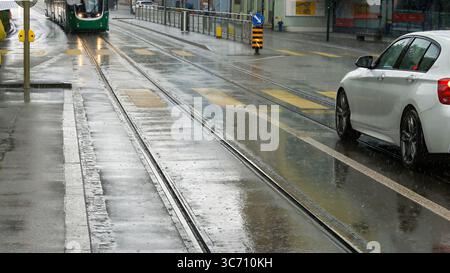 Regnerische City Street Mit Straßenbahnschienen, Modernem Auto Und Nassem Straßenbelag Im Stadtbild Stockfoto