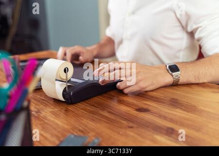 Nahaufnahme der Hände eines anonymen Buchhalters oder Managers, die mit einem Zusatzgerät Ausgaben berechnen, wobei im Büro eine Papierquittung gedruckt wird Stockfoto