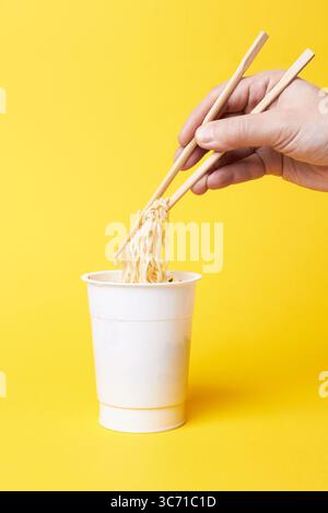 Instant Nudeln und Hand mit Stäbchen auf gelbem Hintergrund Stockfoto