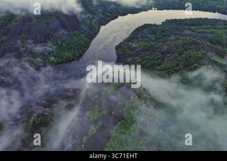 Aus der Vogelperspektive auf den sich windenden Fluss, der durch die üppige grüne Landschaft zieht, umgeben von ätherischem Nebel, Guainia, Guainía, Kolumbien. Stockfoto