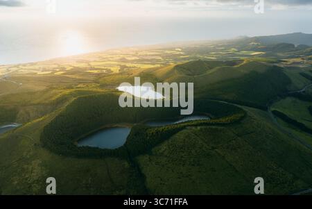 Blick aus der Vogelperspektive auf Zwillingsseen, eingebettet in den grünen vulkanischen Krater, beleuchtet von der goldenen Sonne vor dem fernen Horizont, São Miguel Island, Az Stockfoto