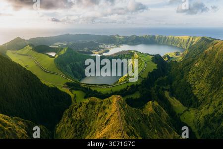 Blick aus der Vogelperspektive auf die Zwillingsseen in einem vulkanischen Krater, wo grüne Hänge das ruhige Wasser unter einem ruhigen Himmel umgeben, Sete Cidades, Portugal. Stockfoto
