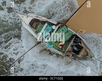 Aus der Vogelperspektive eines Fischerbootes mit grünen Netzen, die am Sandstrand liegen, während Wellen um ihn herum krachen, Praia de Mira, Coimbra, Portugal. Stockfoto