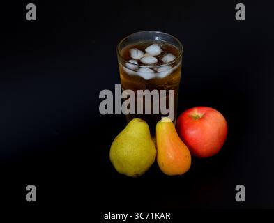 Apfel- und Birnensaft mit Eis in einem hohen Glas auf schwarzem Hintergrund, reife Früchte verschiedener Sorten in der Nähe. Nahaufnahme. Stockfoto