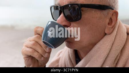 Ein älterer Mann mit Sonnenbrille schlürft aus einem Becher und genießt seinen Drink. Stockfoto