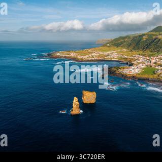Aus der Vogelperspektive treffen auf das tiefblaue Meer, mit dem Dorf an grünen Hängen, Ilhéus dos Mosteiros, Mosteiros, Portugal. Stockfoto